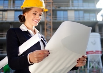 Grupo Albatros. Mujer arquitecta en obra leyendo plano en sus manos y con casco amarillo
